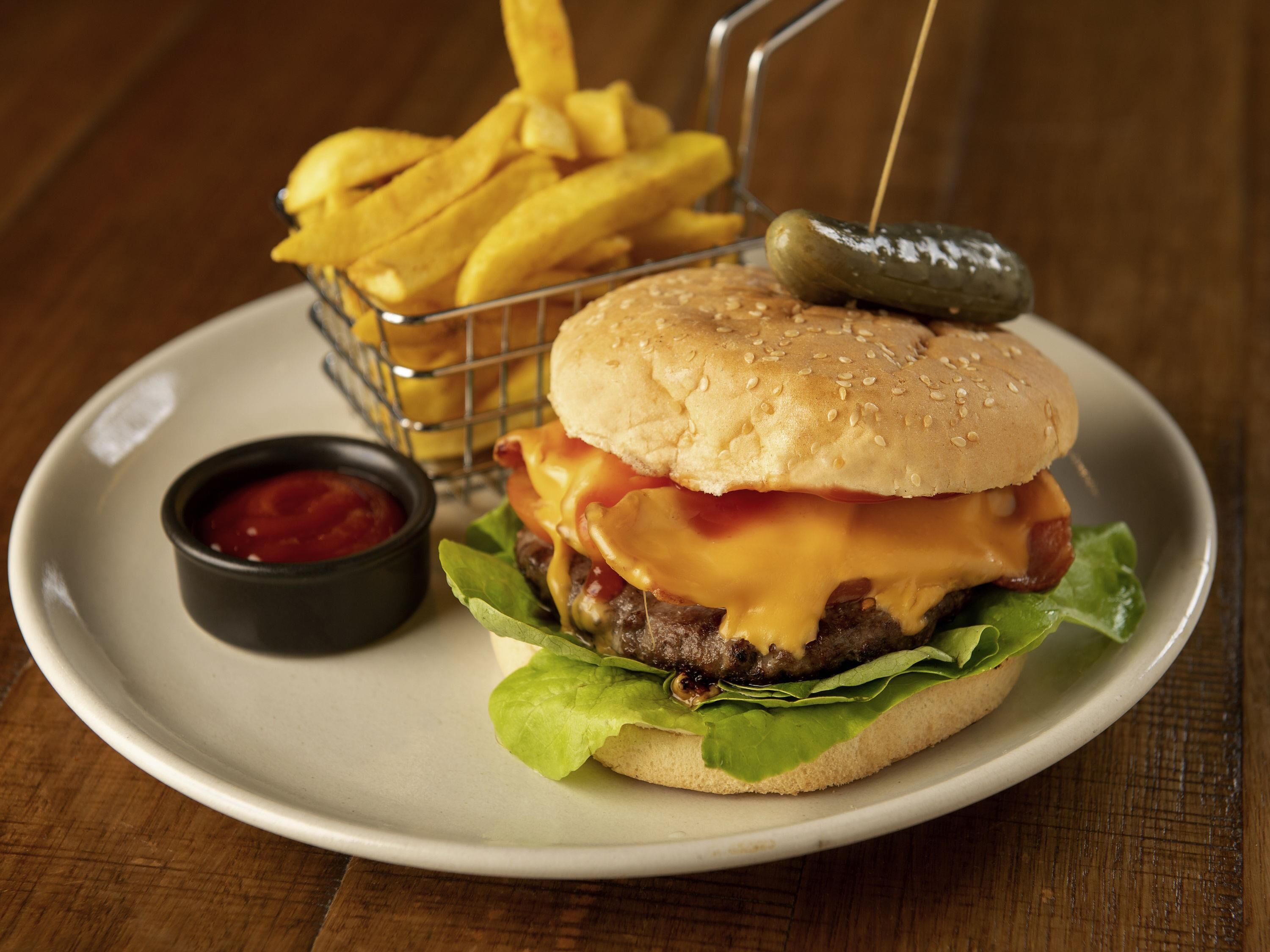 A burger with cheese, lettuce, and a bun, served with fries and a pickle on a plate.