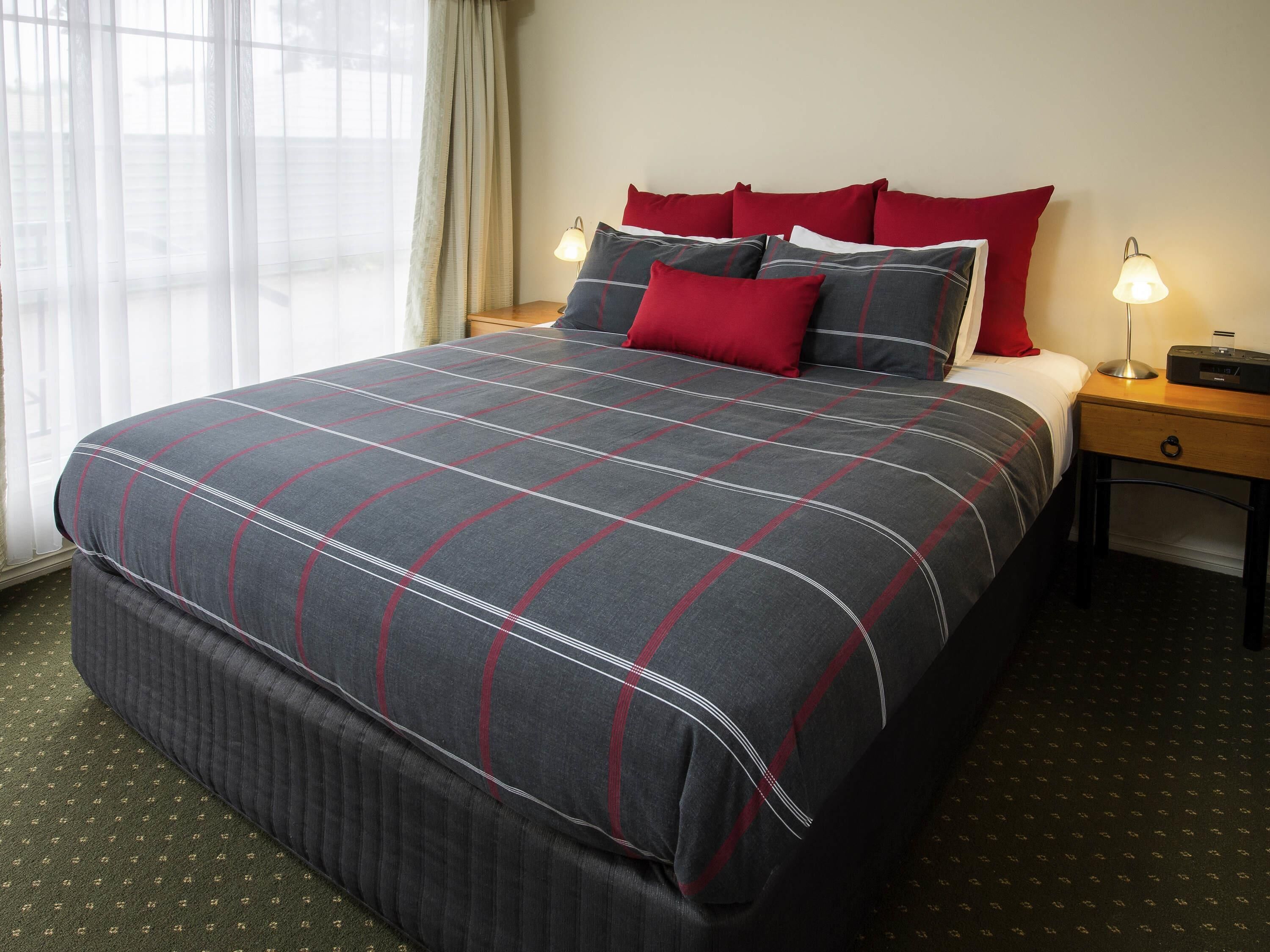 A neatly made bed with a striped bedspread, two bedside tables with lamps, and a window with curtains.