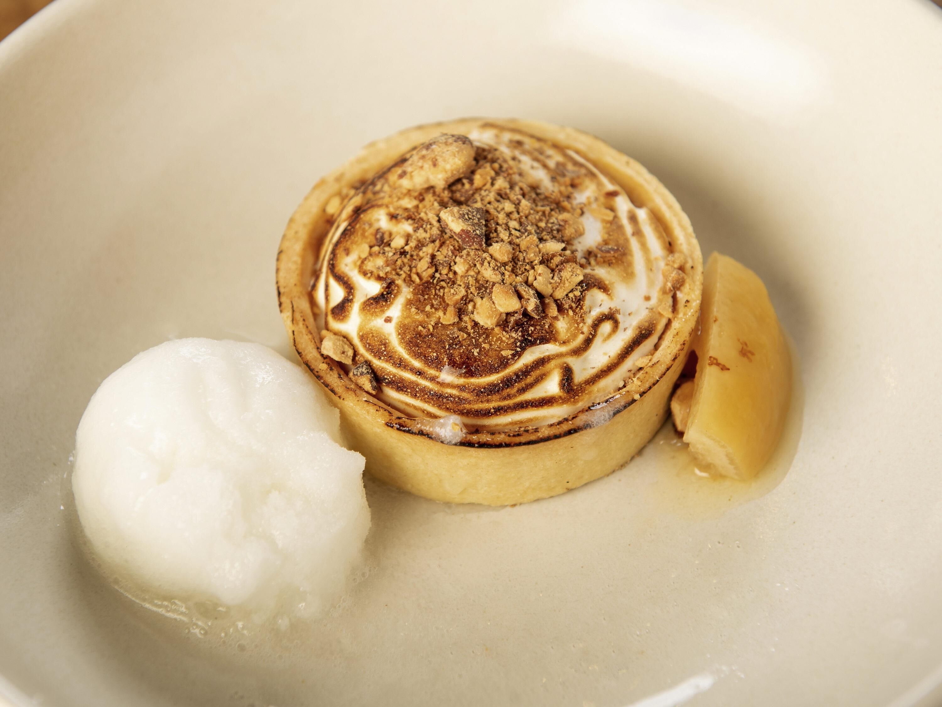 A dessert with a golden-brown top, a dollop of white cream, and a piece of fruit on a plate.