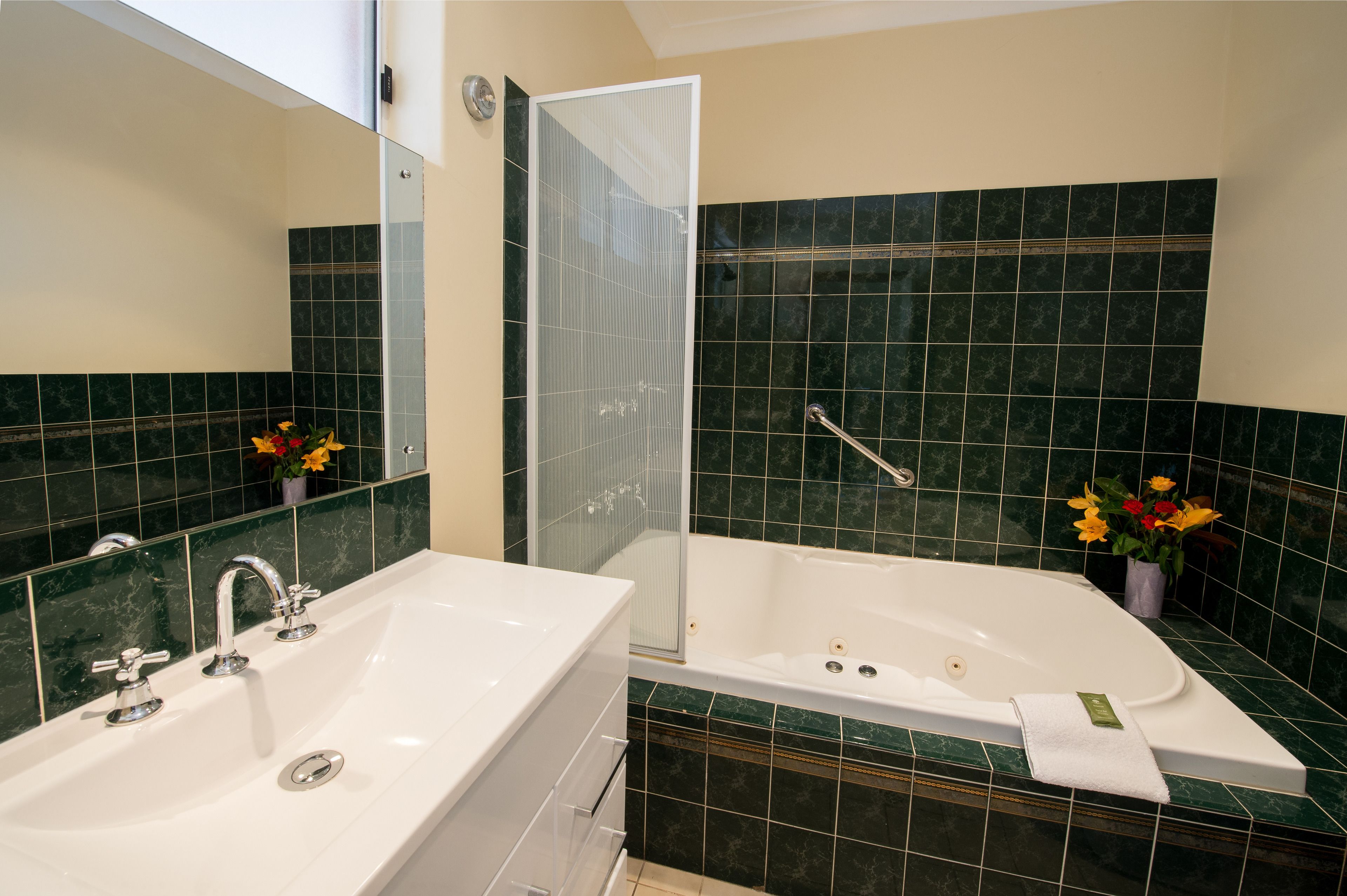 Un baño con un lavamanos blanco, una bañera y una ducha. Las paredes están cubiertas de azulejos verdes y hay un espejo sobre el lavamanos.