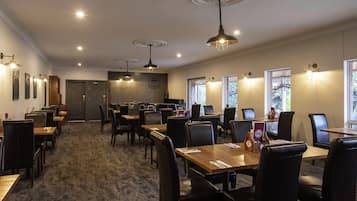 Un restaurant avec plusieurs tables et chaises, des luminaires au plafond et une porte visible au fond.