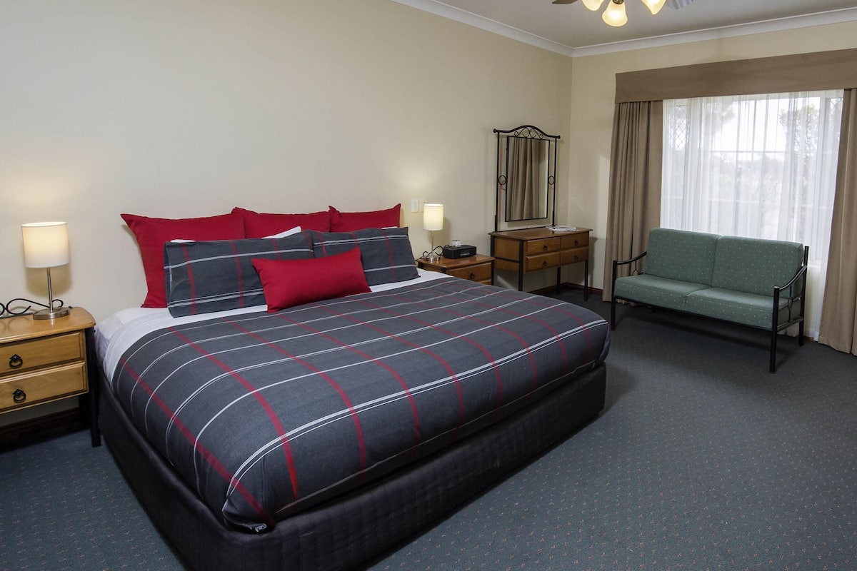 A hotel room with a large bed, bedside tables, a desk, a chair, a mirror, and a window with curtains.