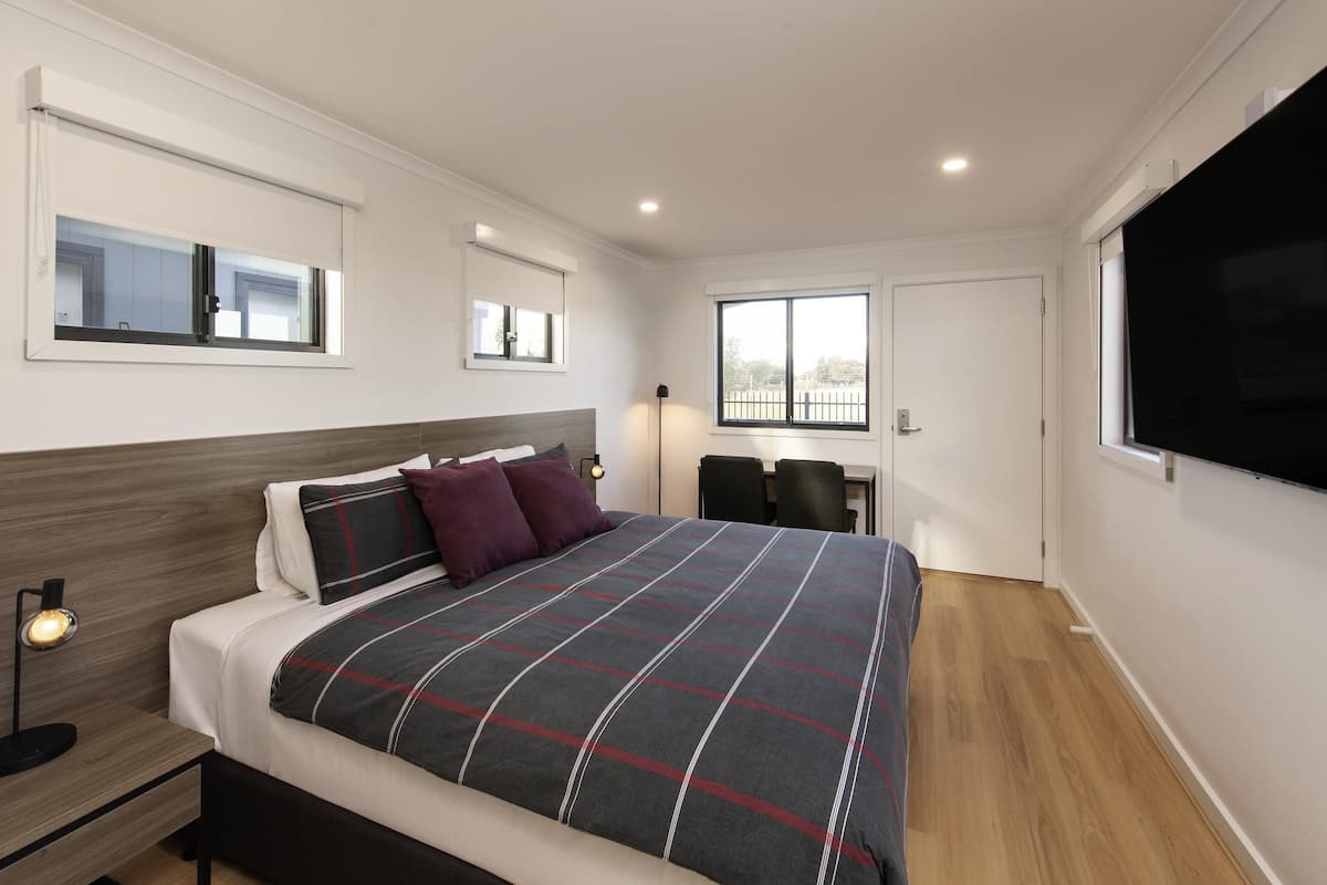 A modern bedroom with a bed, bedside tables, a desk, and a TV.