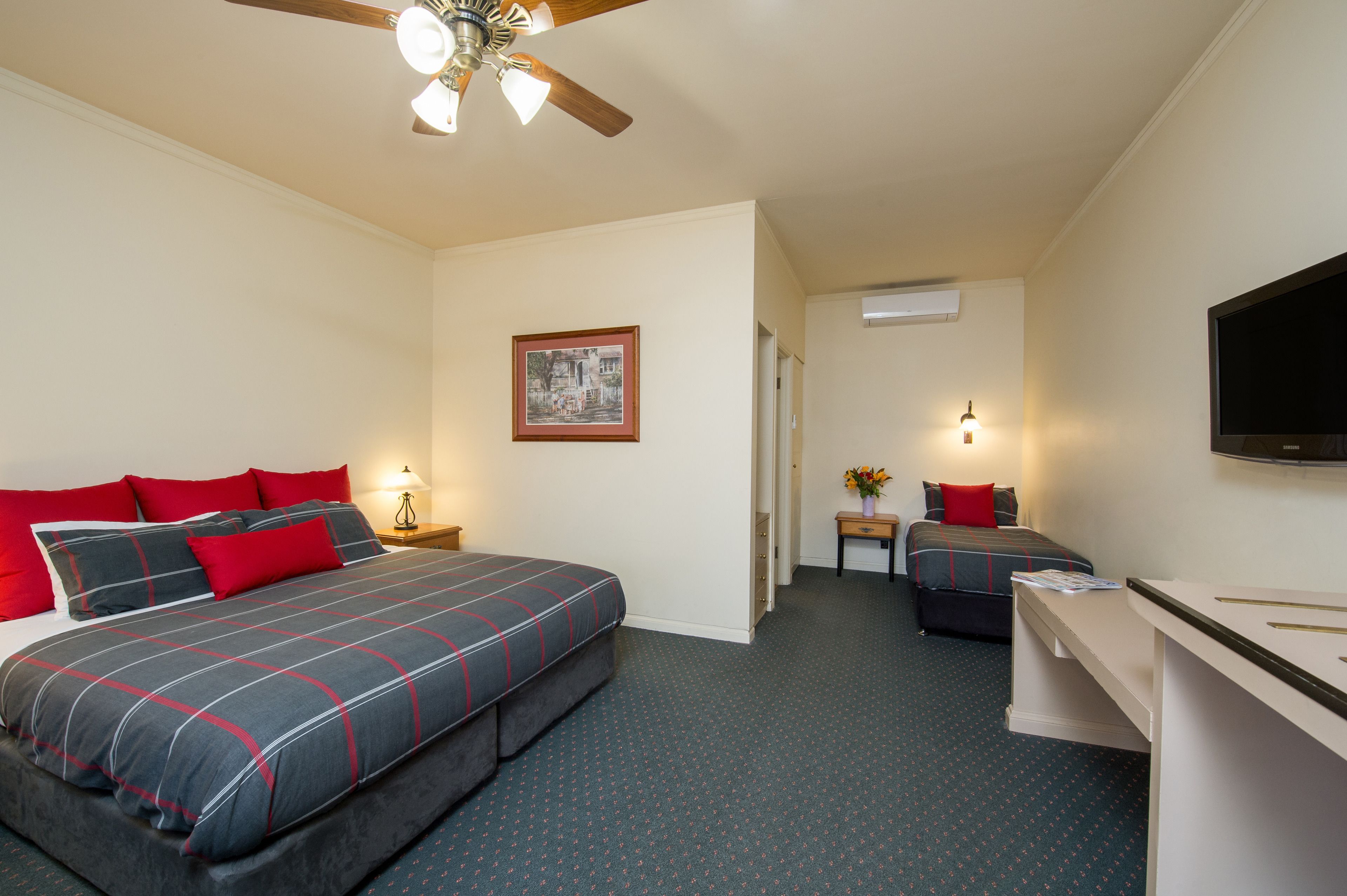 A hotel room with a large bed, a smaller bed, a desk, and a ceiling fan.