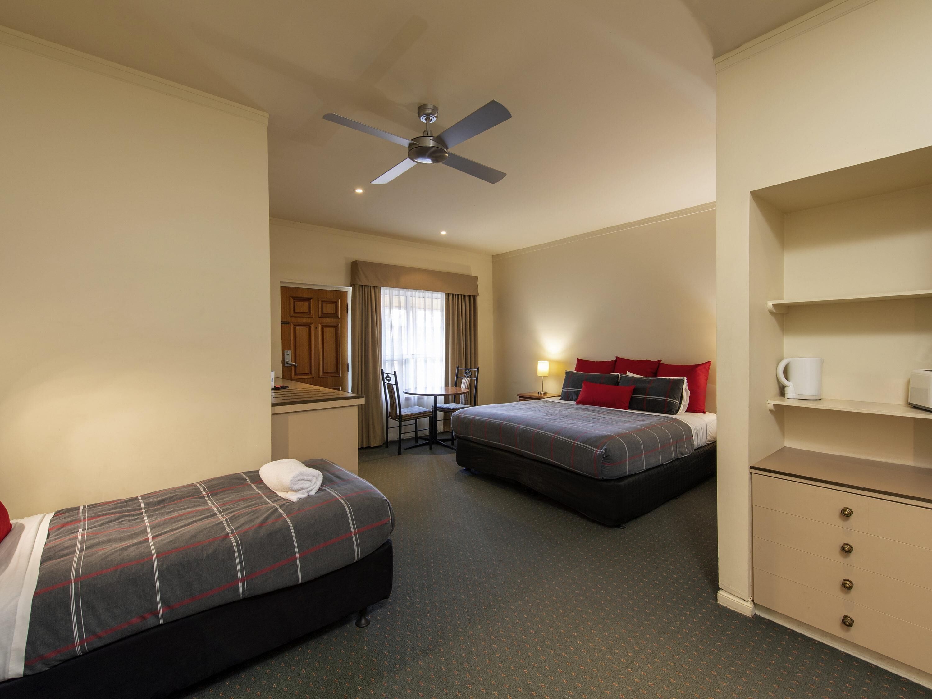 A hotel room with two beds, a desk, a chair, a ceiling fan, and a minibar.