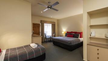 A hotel room with two beds, a desk, a chair, a ceiling fan, and a minibar.