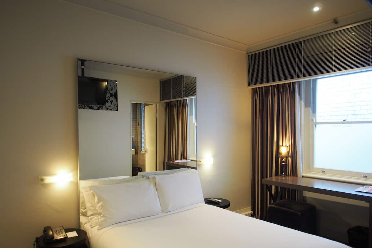 Una habitación de hotel con cama, escritorio, silla, teléfono, espejo y ventana con cortinas.