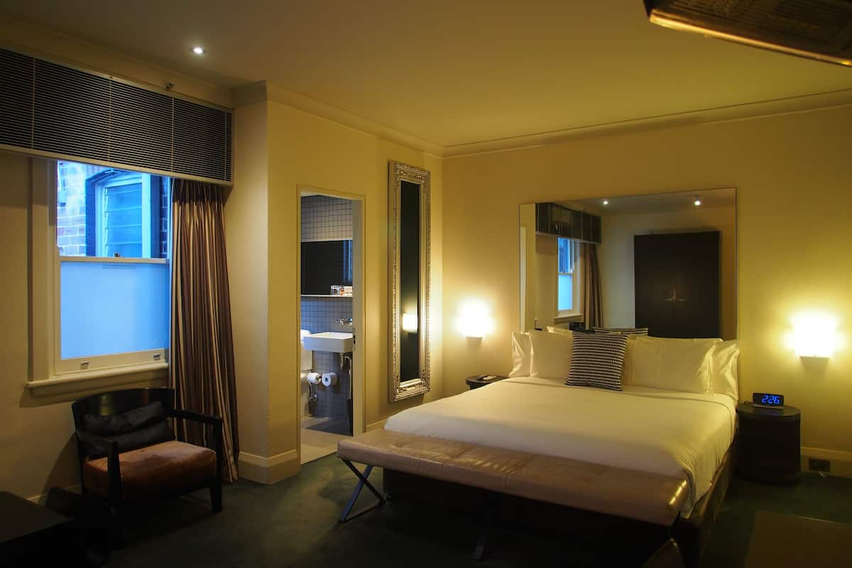 Habitación de hotel con una cama grande, una silla, un escritorio, un espejo y una ventana con cortinas.