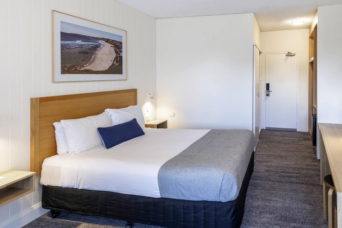 A neatly made bed with a wooden headboard, a bedside table with a lamp, and a framed picture on the wall.