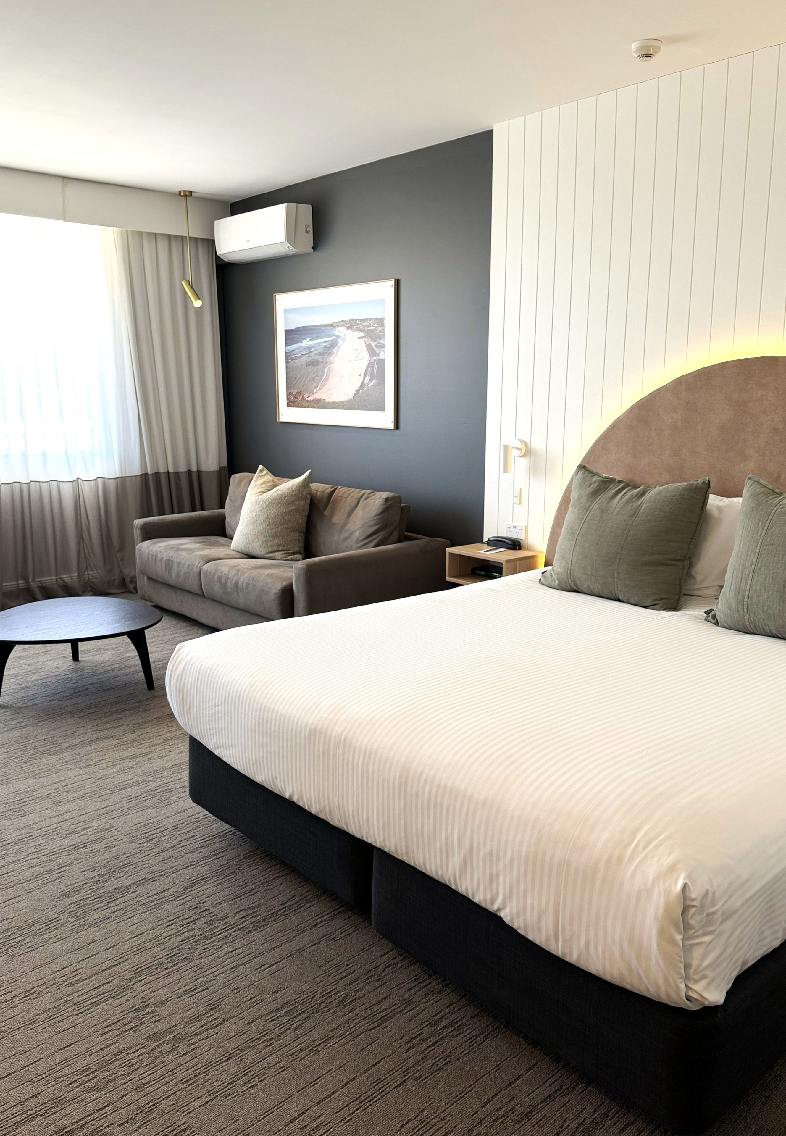 Een hotelkamer met een groot bed, een bank, een kleine tafel en een ingelijste foto aan de muur.