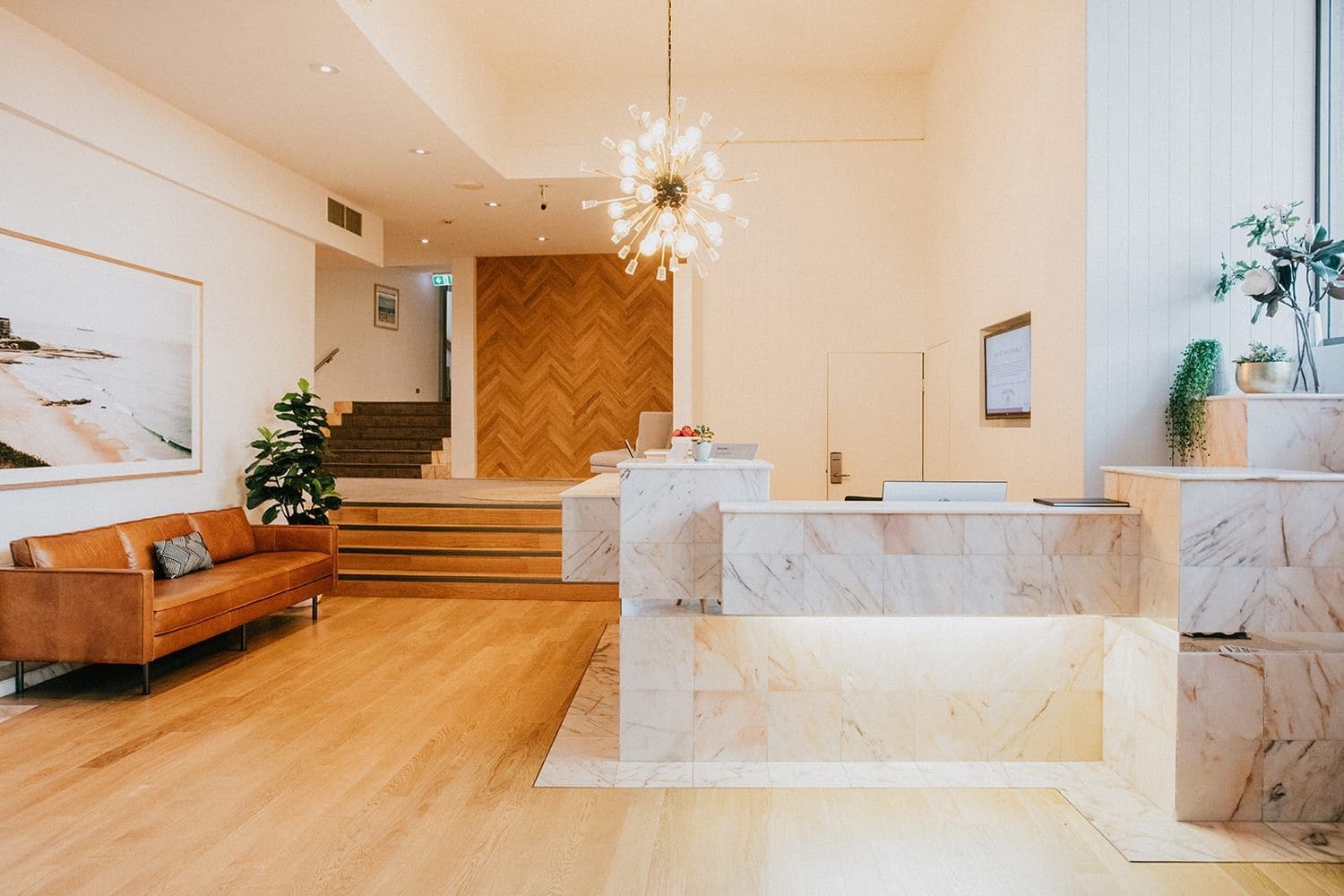 Un moderno vestíbulo de hotel con una recepción, un sofá, una escalera y un gran ventanal.