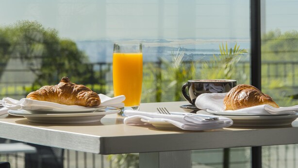 A breakfast table with croissants, a glass of orange juice, and a cup, set against a scenic view. - Mercure Charlestown (Adamstown Heights)