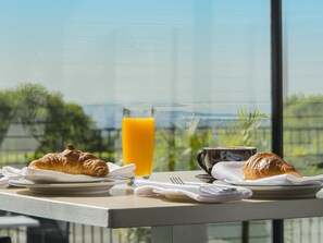A breakfast table with croissants, a glass of orange juice, and a cup, set against a scenic view. - Mercure Charlestown (Adamstown Heights)