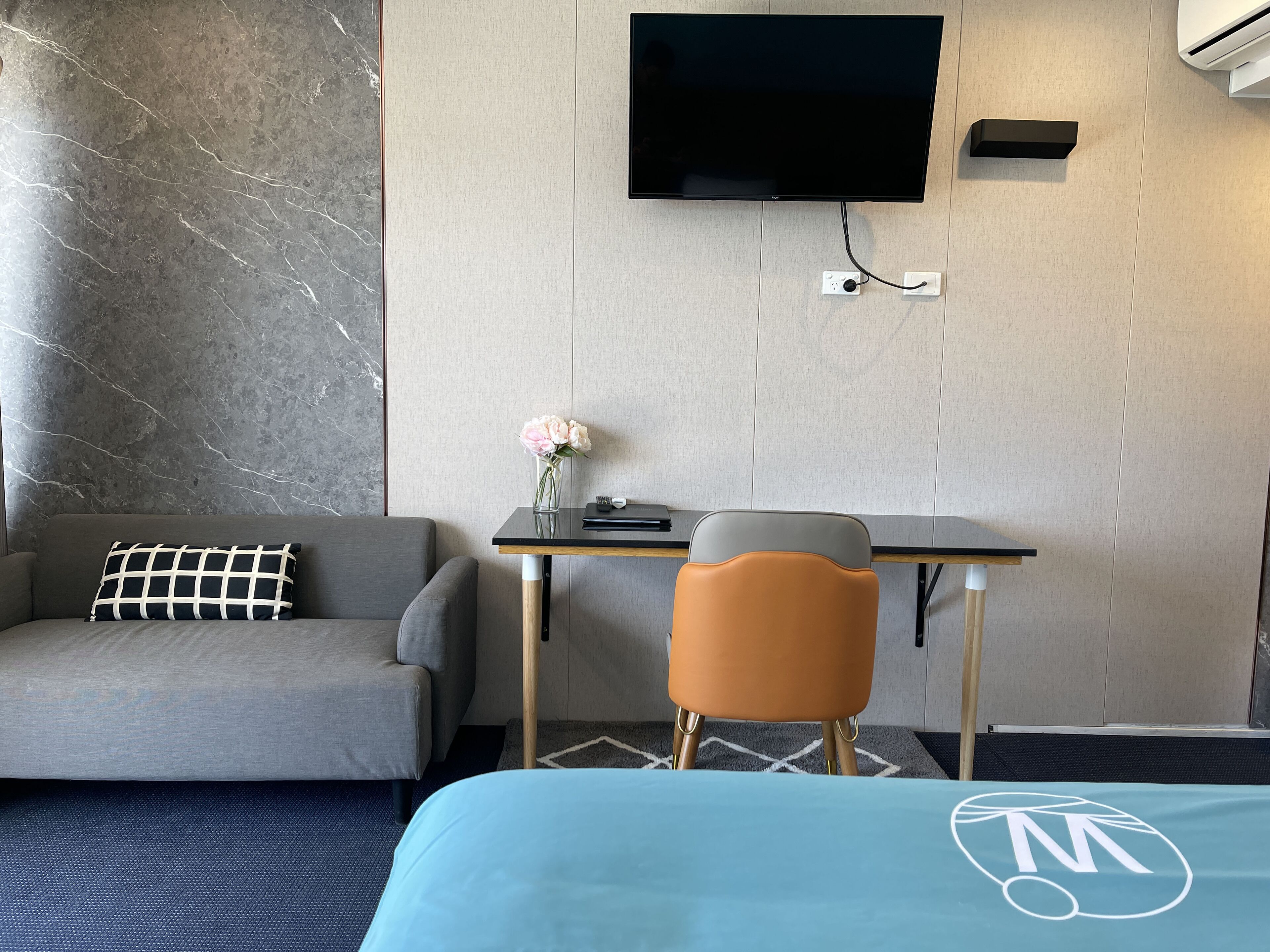 A hotel room with a bed, a desk, a chair, a sofa, a TV, and a vase with flowers.
