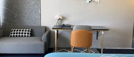 A hotel room with a bed, a desk, a chair, a sofa, a TV, and a vase with flowers.