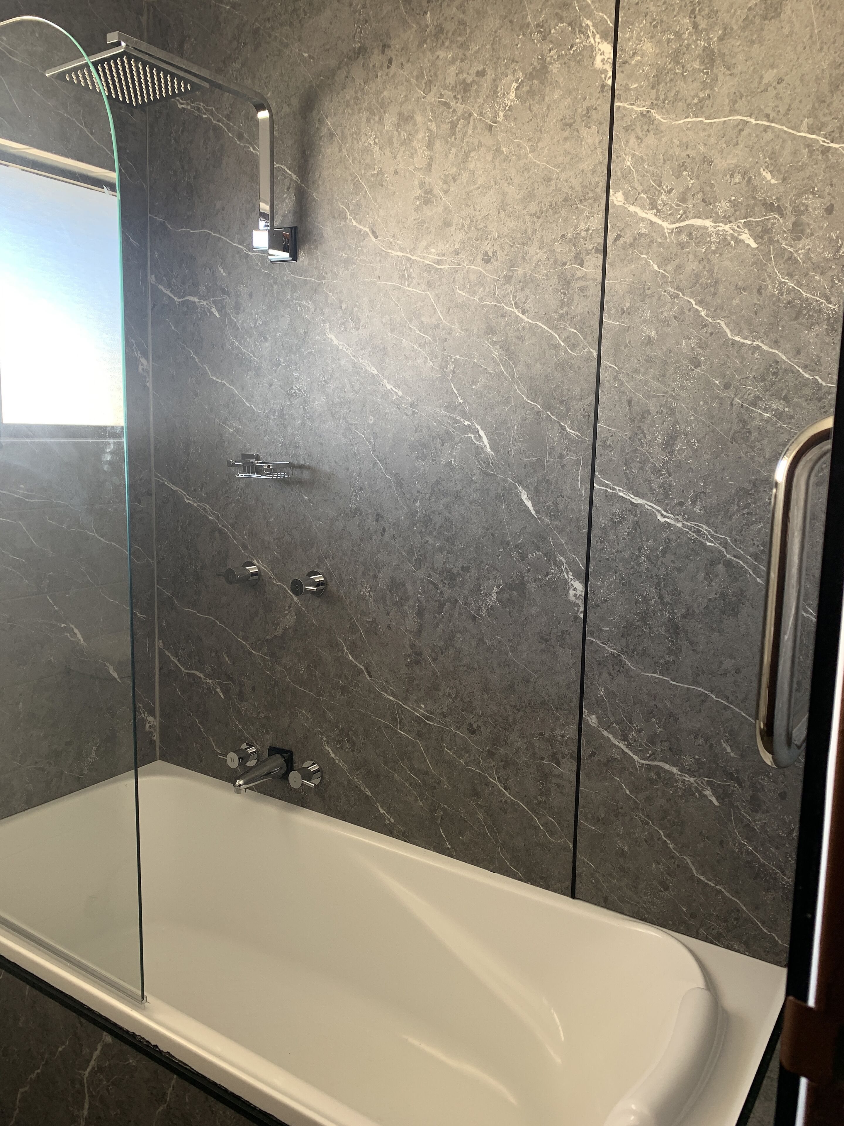Un baño moderno con cabina de ducha de vidrio, una bañera blanca y paredes de mármol oscuro.