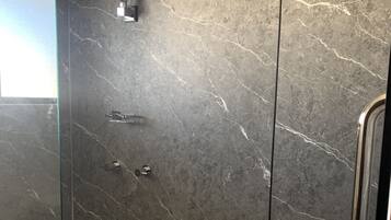 Un baño moderno con cabina de ducha de vidrio, una bañera blanca y paredes de mármol oscuro.
