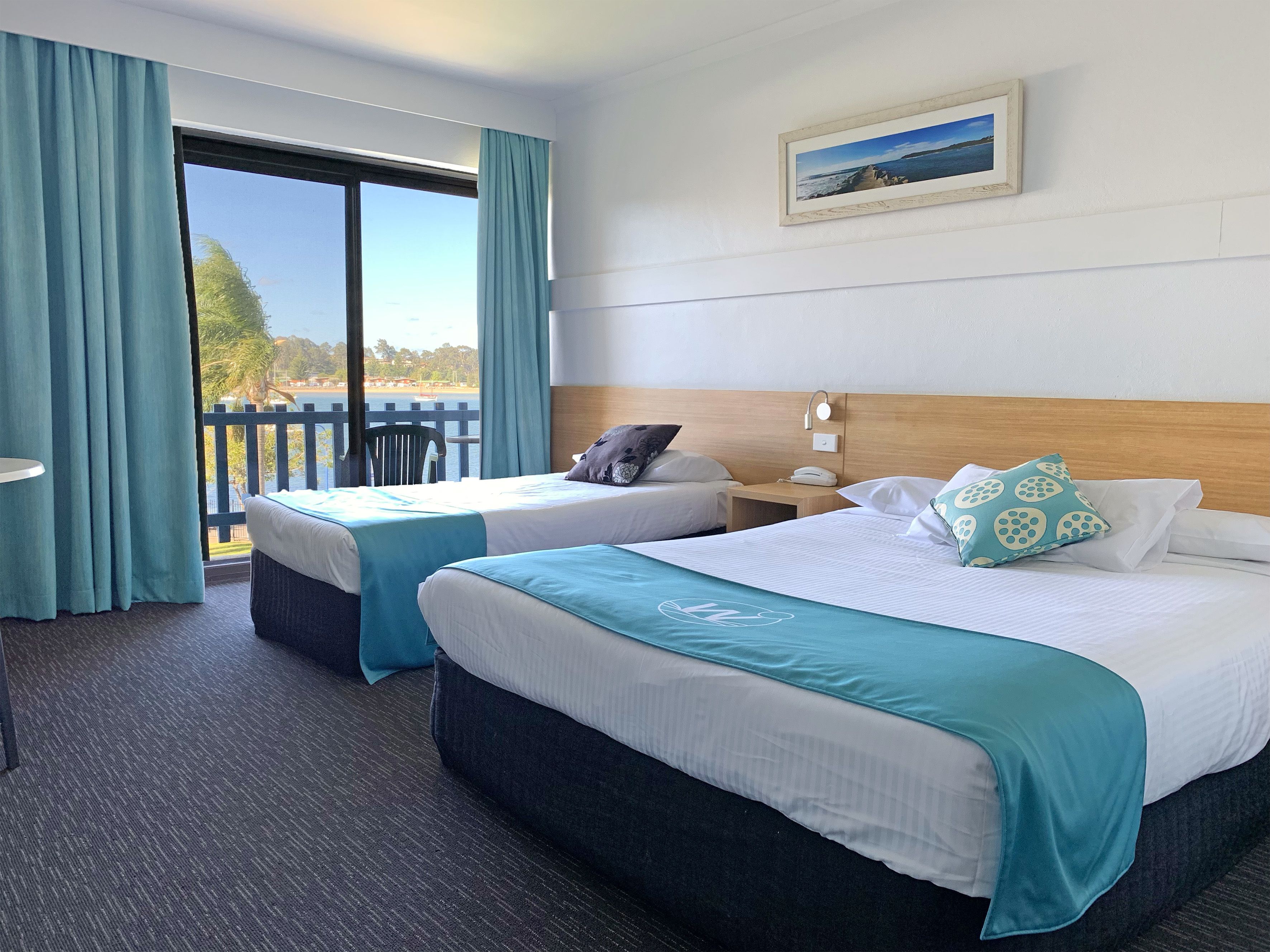 A hotel room with two beds, a desk, and a view of the sea.