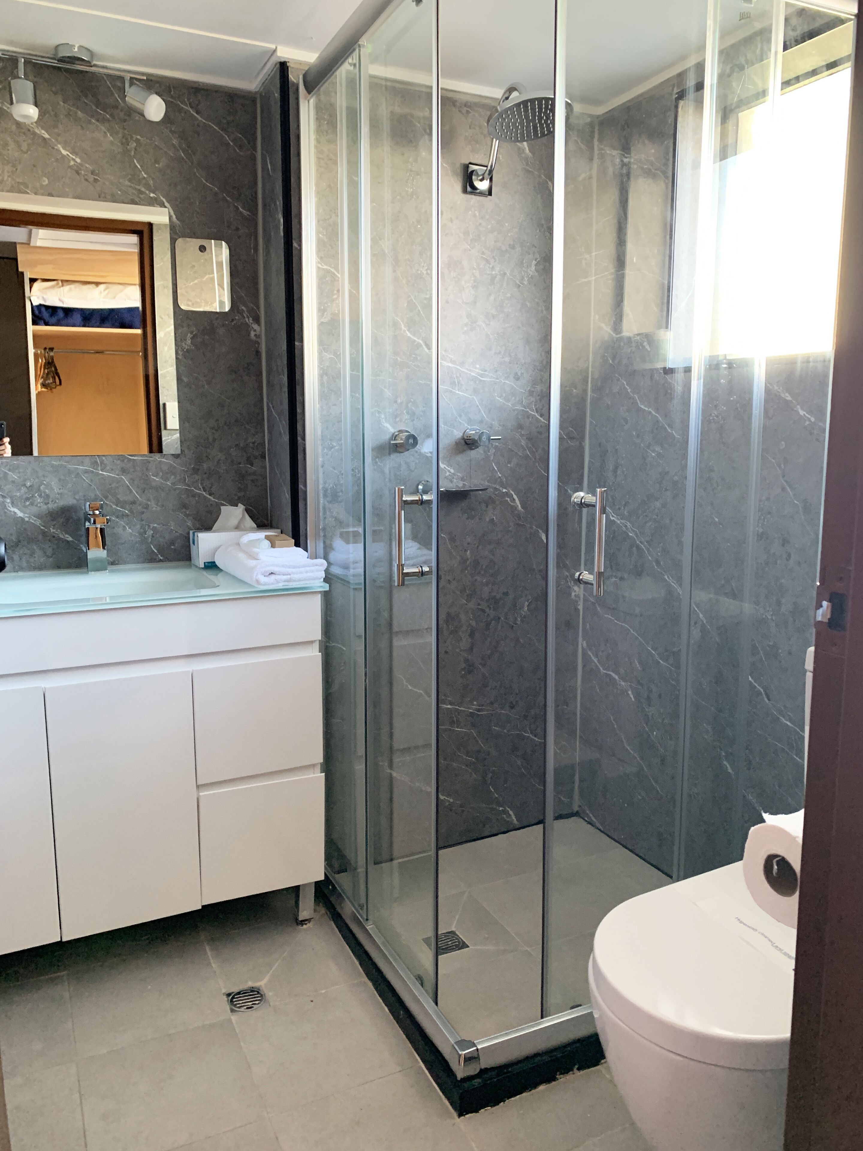 A modern bathroom with a glass-enclosed shower, a white toilet, and a marble-tiled vanity.