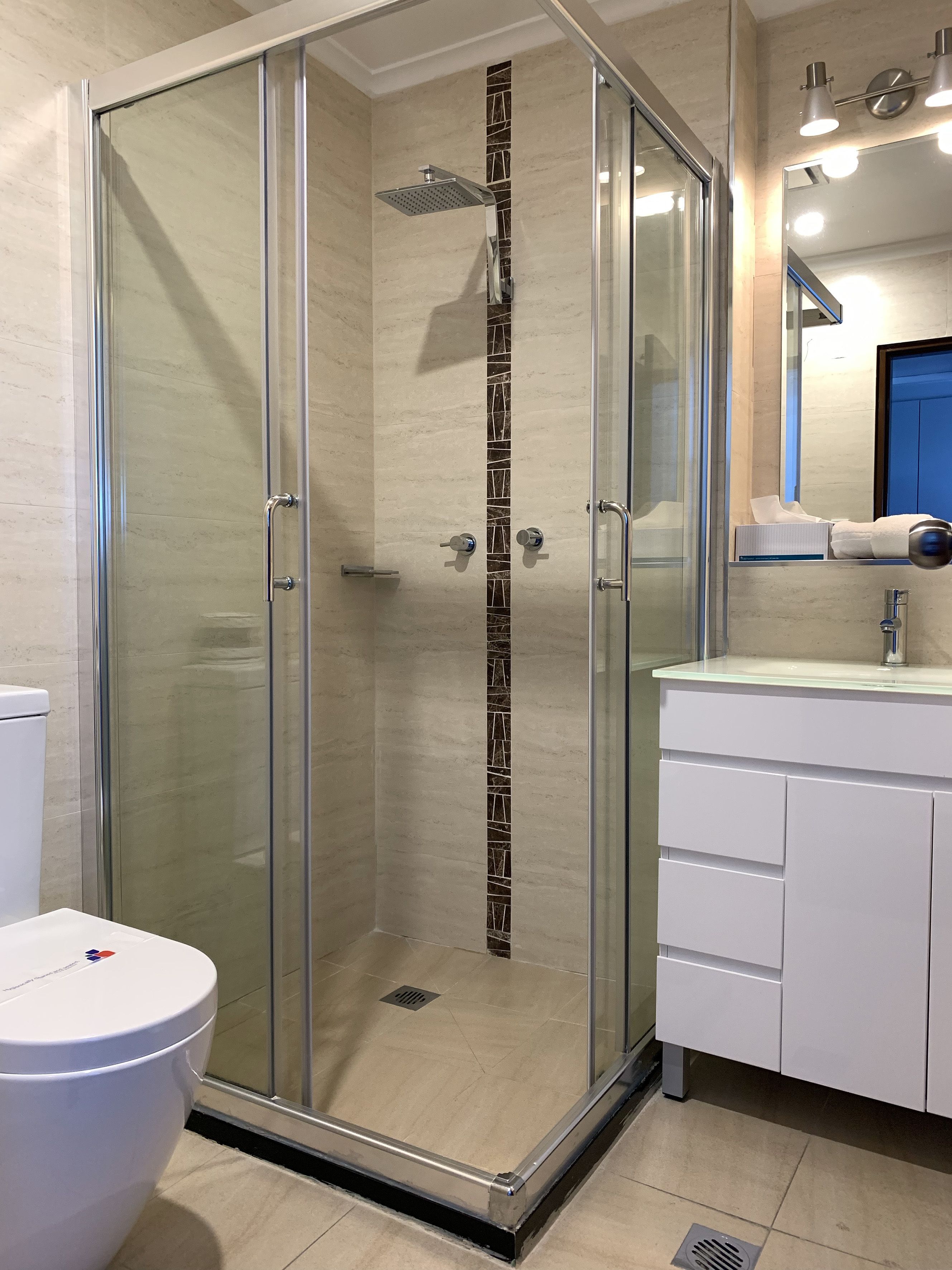 Ein modernes Badezimmer mit einer Glaskabine zur Dusche, einer weißen Toilette und einem Waschtisch mit Schränken.