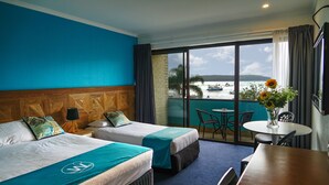 A hotel room with two beds, a balcony with a view of the sea, a table, and a chair.