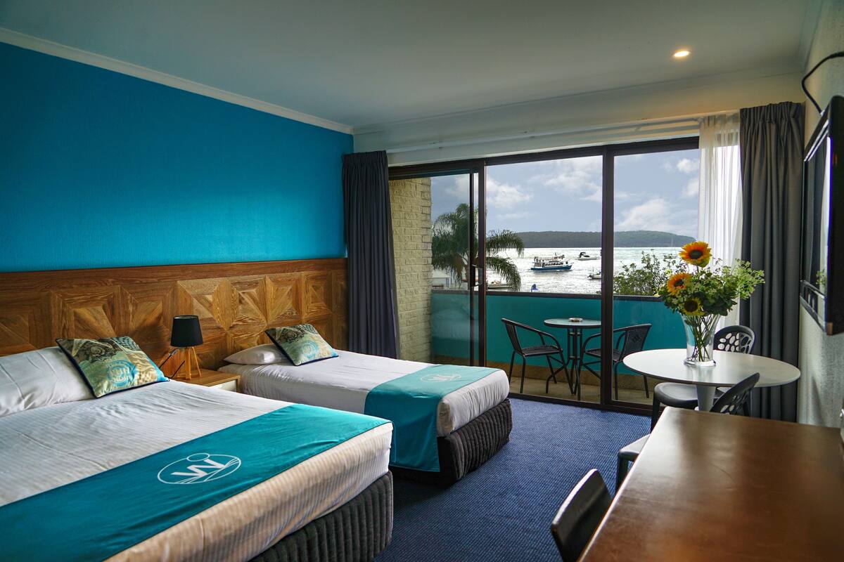 A hotel room with two beds, a balcony with a view of the sea, a table, and a chair.