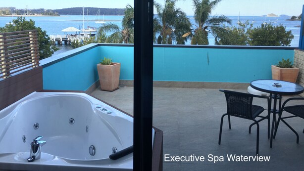 A spa suite with a large bathtub, a small table, two chairs, and a view of the water and boats.