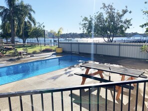 Relax by the pool surrounded by lush greenery and a serene body of water.