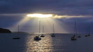 A calm sea with several sailboats anchored, under a cloudy sky with sunlight breaking through.
