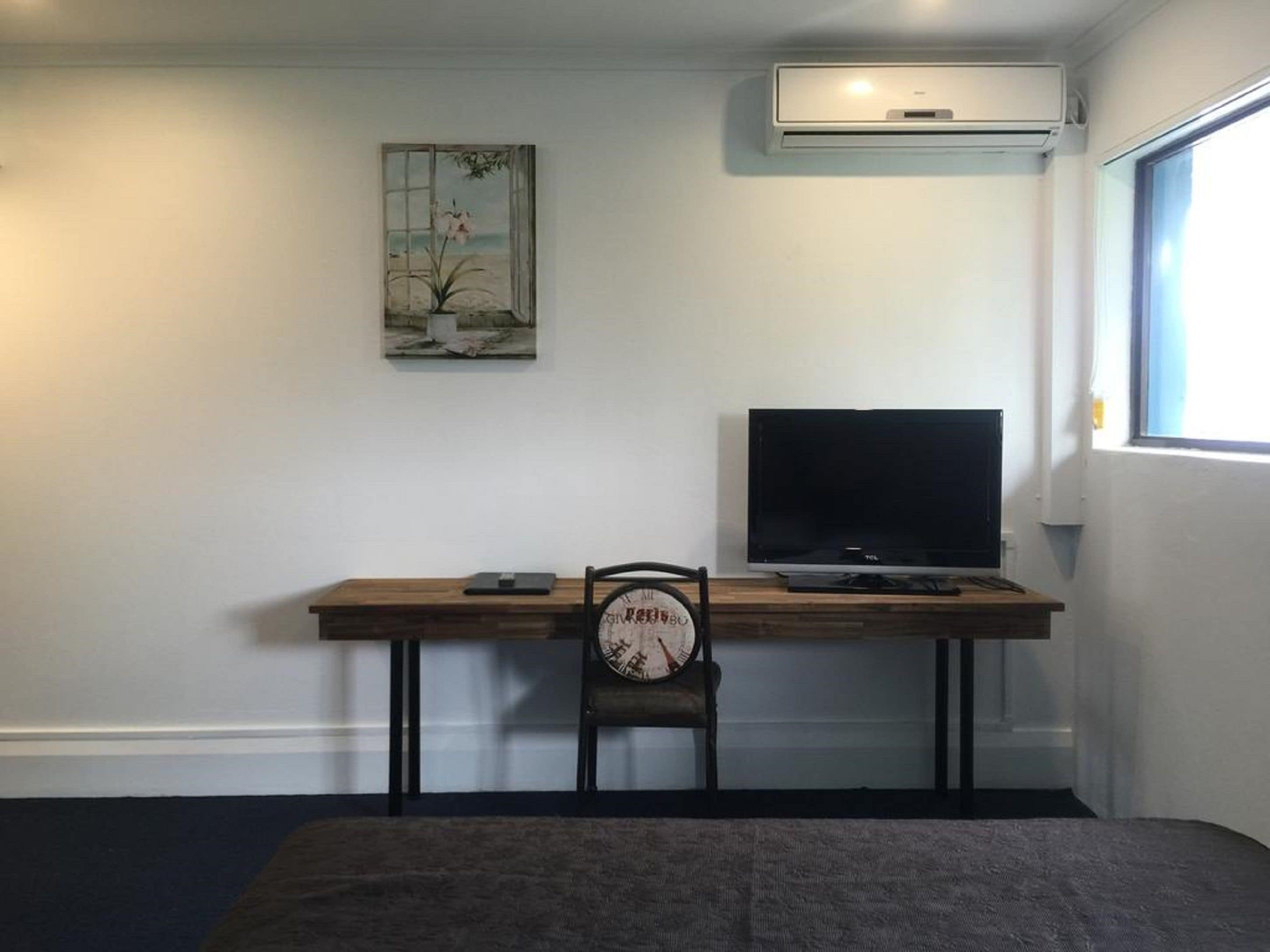 Una habitación con escritorio de madera, una silla, un televisor de pantalla plana, aire acondicionado y una ventana con vistas.