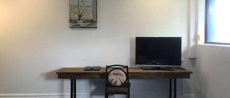 Una habitación con escritorio de madera, una silla, un televisor de pantalla plana, aire acondicionado y una ventana con vistas.
