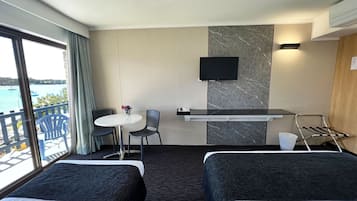 Habitación de hotel con dos camas, una mesita con sillas, un televisor y vista al mar.