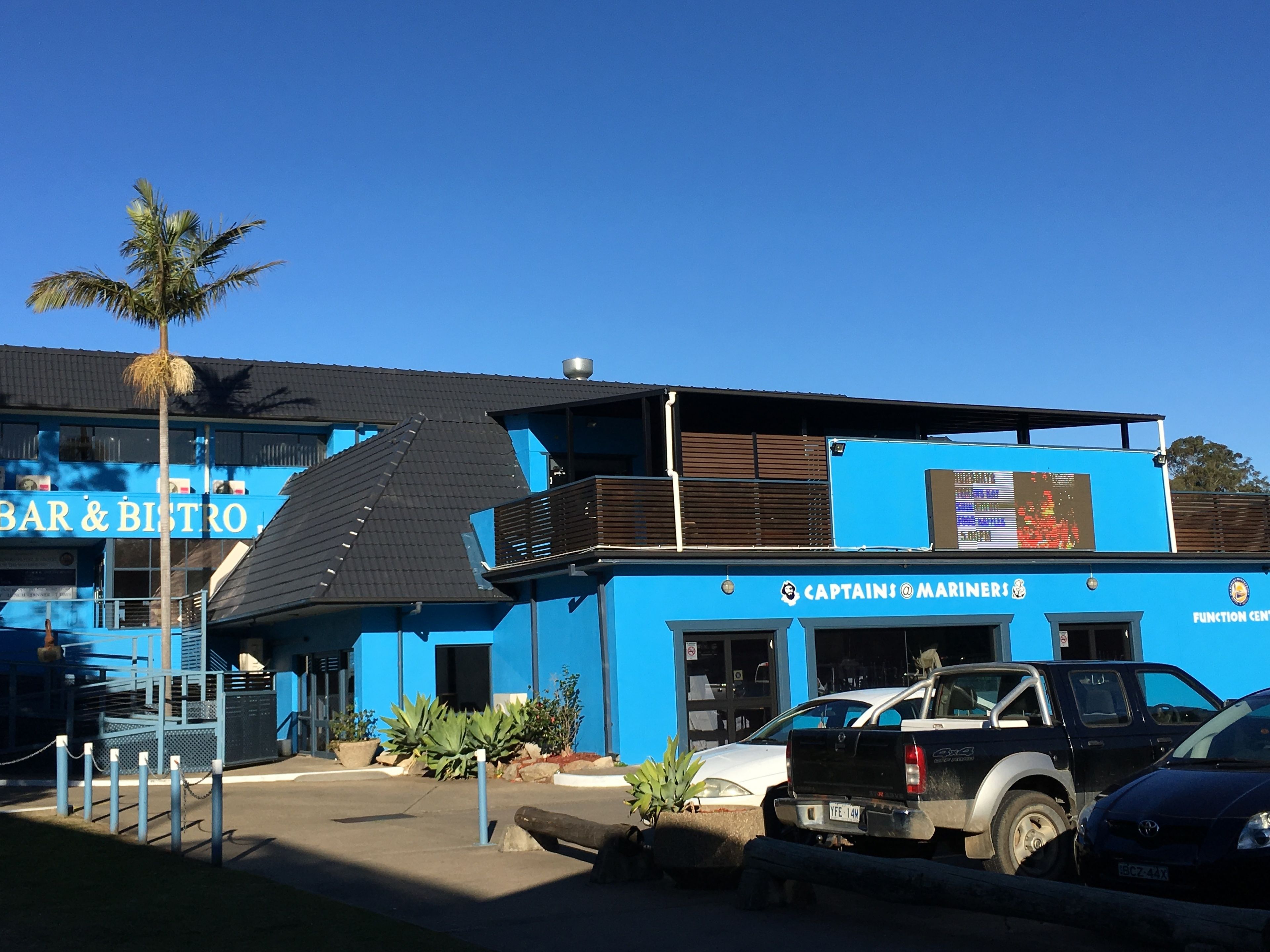 Un bâtiment bleu avec une enseigne indiquant « BAR ET BISTROT » et « CAPTAINS @ MARINERS ».