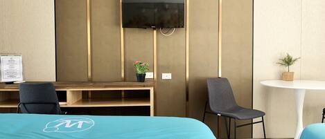 Habitación de hotel con cama, escritorio, silla, televisión y una mesita con una planta.