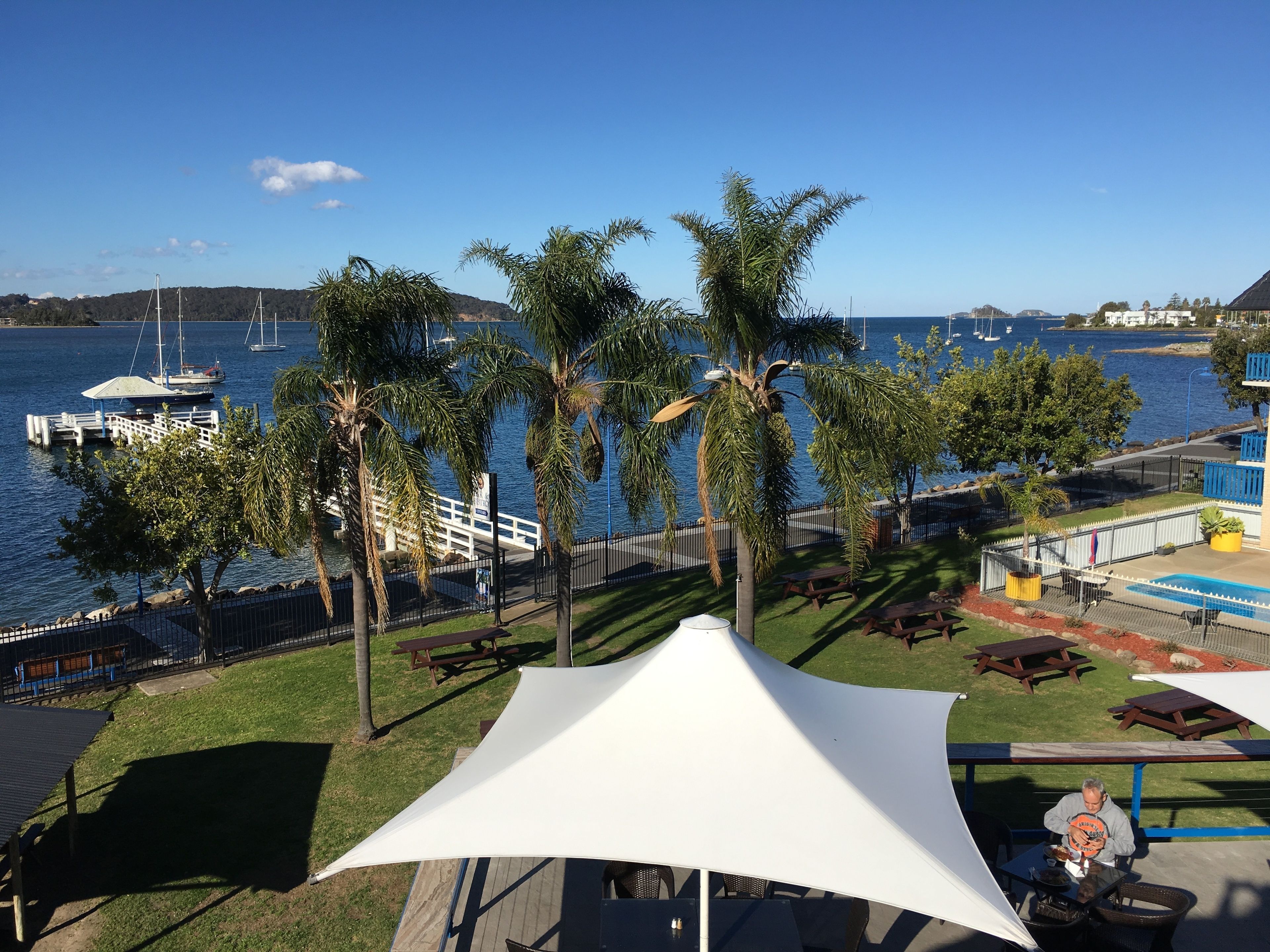 A waterfront patio with palm trees, a white canopy, and a view of the marina.