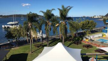 A waterfront patio with palm trees, a white canopy, and a view of the marina.