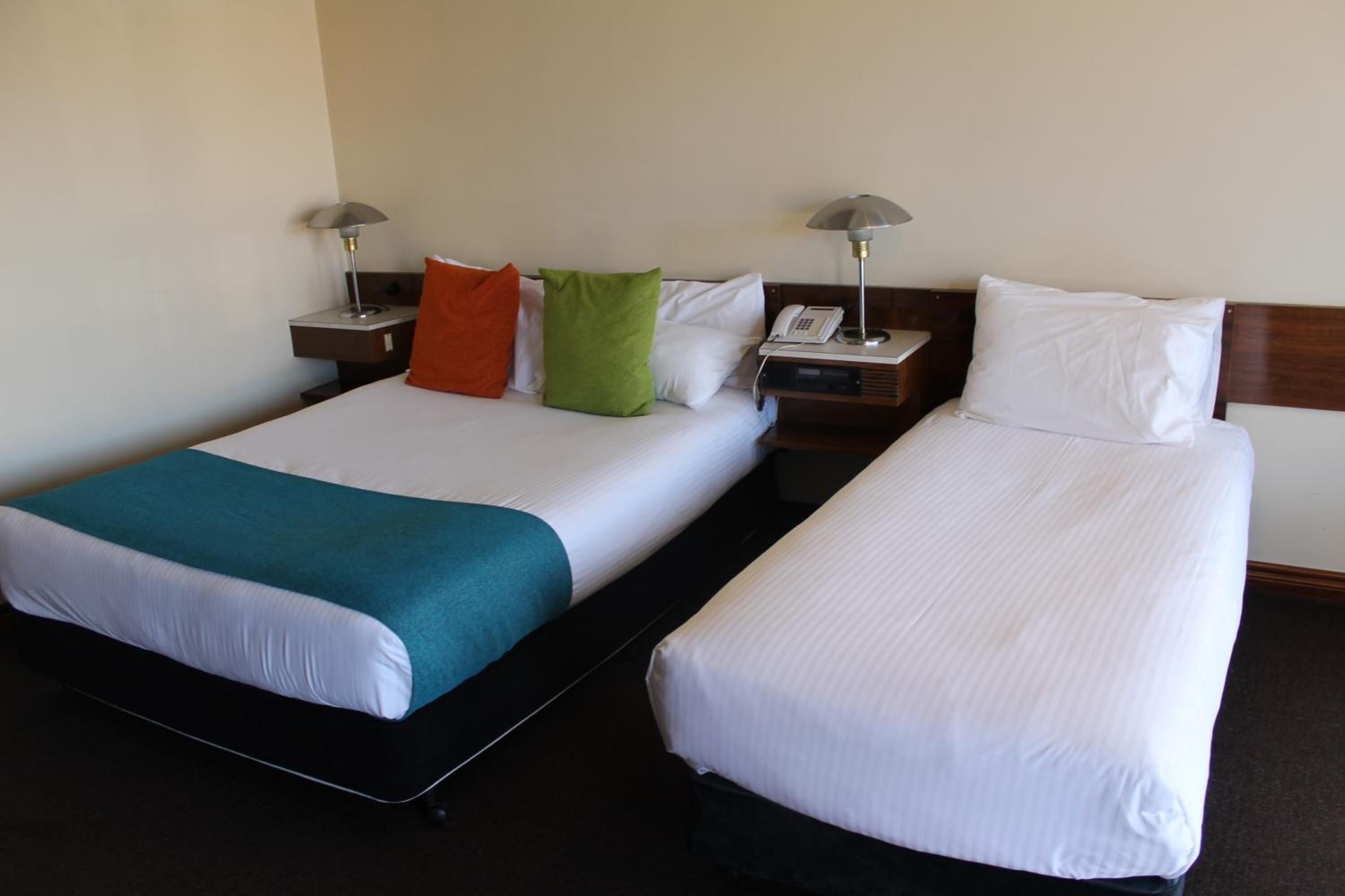 Two single beds with white linens, a teal throw blanket on the left bed, and a green pillow on the right bed. Each bed has a nightstand with a lamp and a telephone.