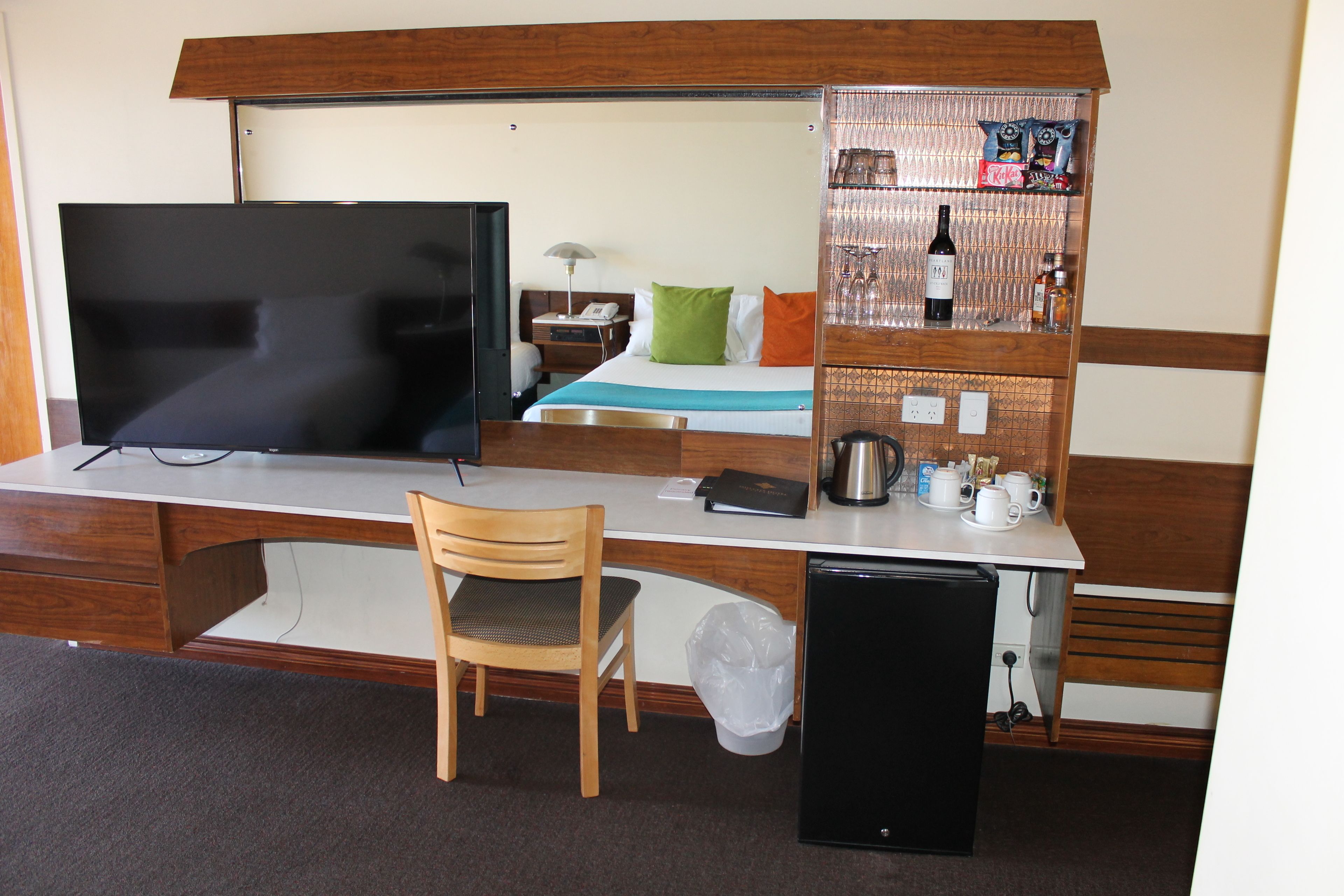 A hotel room with a bed, a desk with a television, a chair, a small refrigerator, and a minibar.