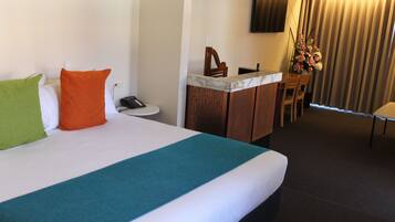 A hotel room with a large bed, a desk with a chair, a TV mounted on the wall, and a window with curtains.