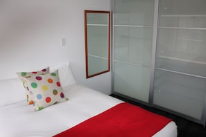 Ein Hotelzimmer mit einem Bett, weißer Bettwäsche, einer roten Tagesdecke und einem farbenfrohen, gepunkteten Kissen.