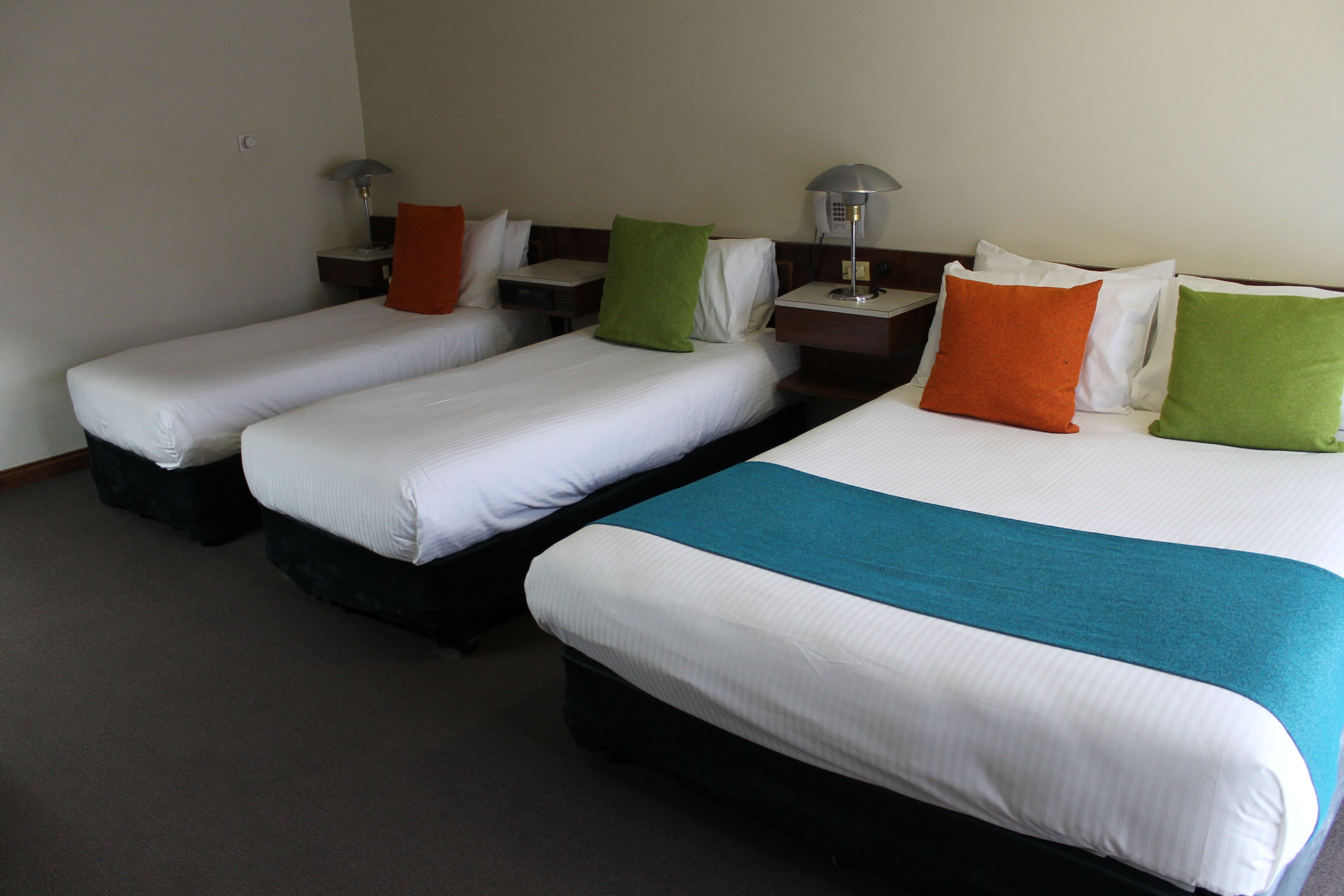 Habitación de hotel con tres camas individuales, cada una con una almohada y una mesita de noche.