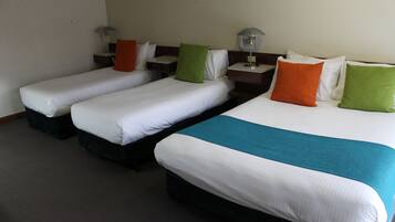 Habitación de hotel con tres camas individuales, cada una con una almohada y una mesita de noche.