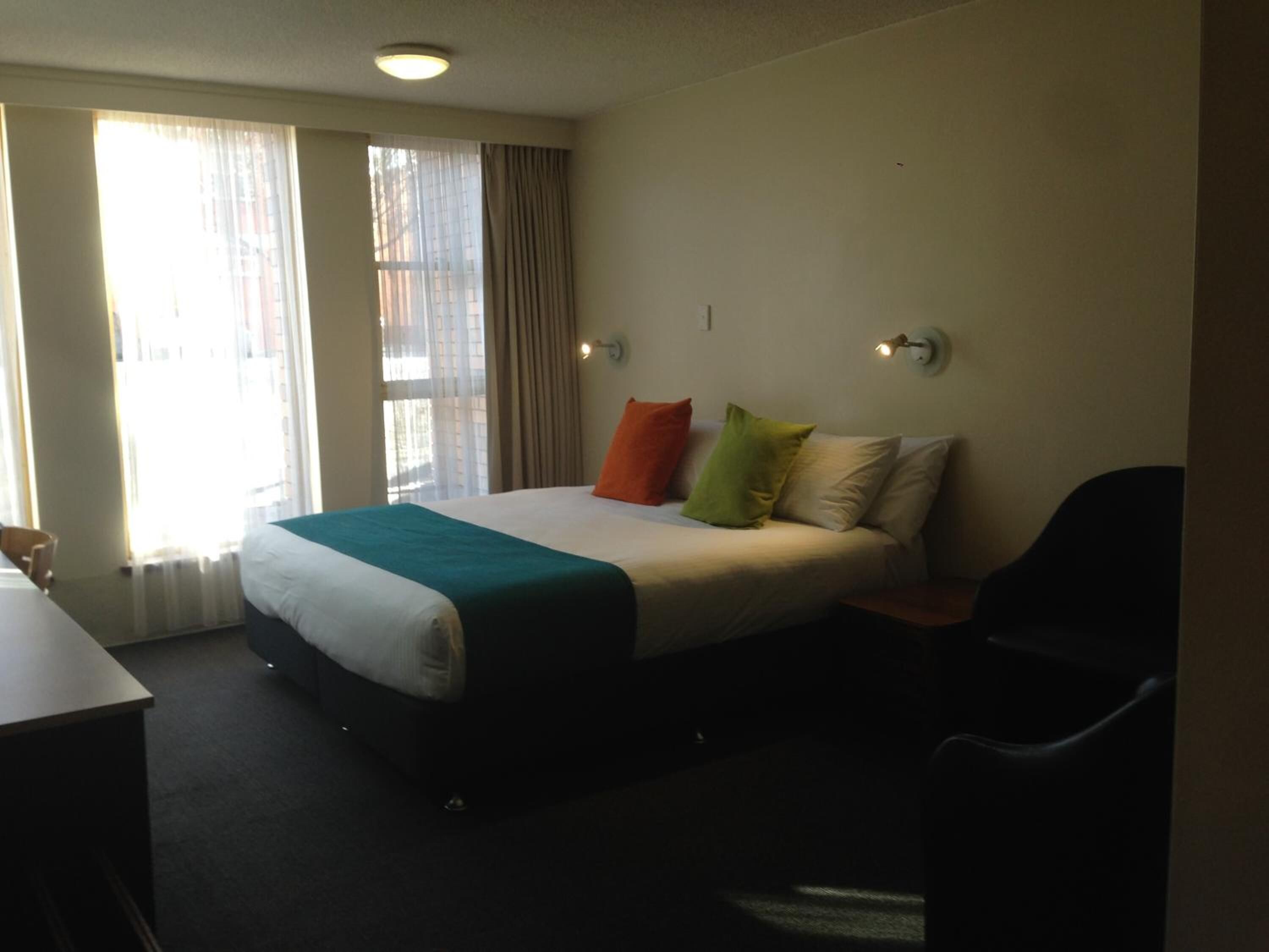A hotel room with a bed, a desk, a chair, and a window with curtains.
