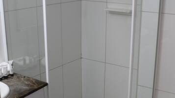 A bathroom with a white tiled floor, a glass shower enclosure, and a marble countertop with toiletries.