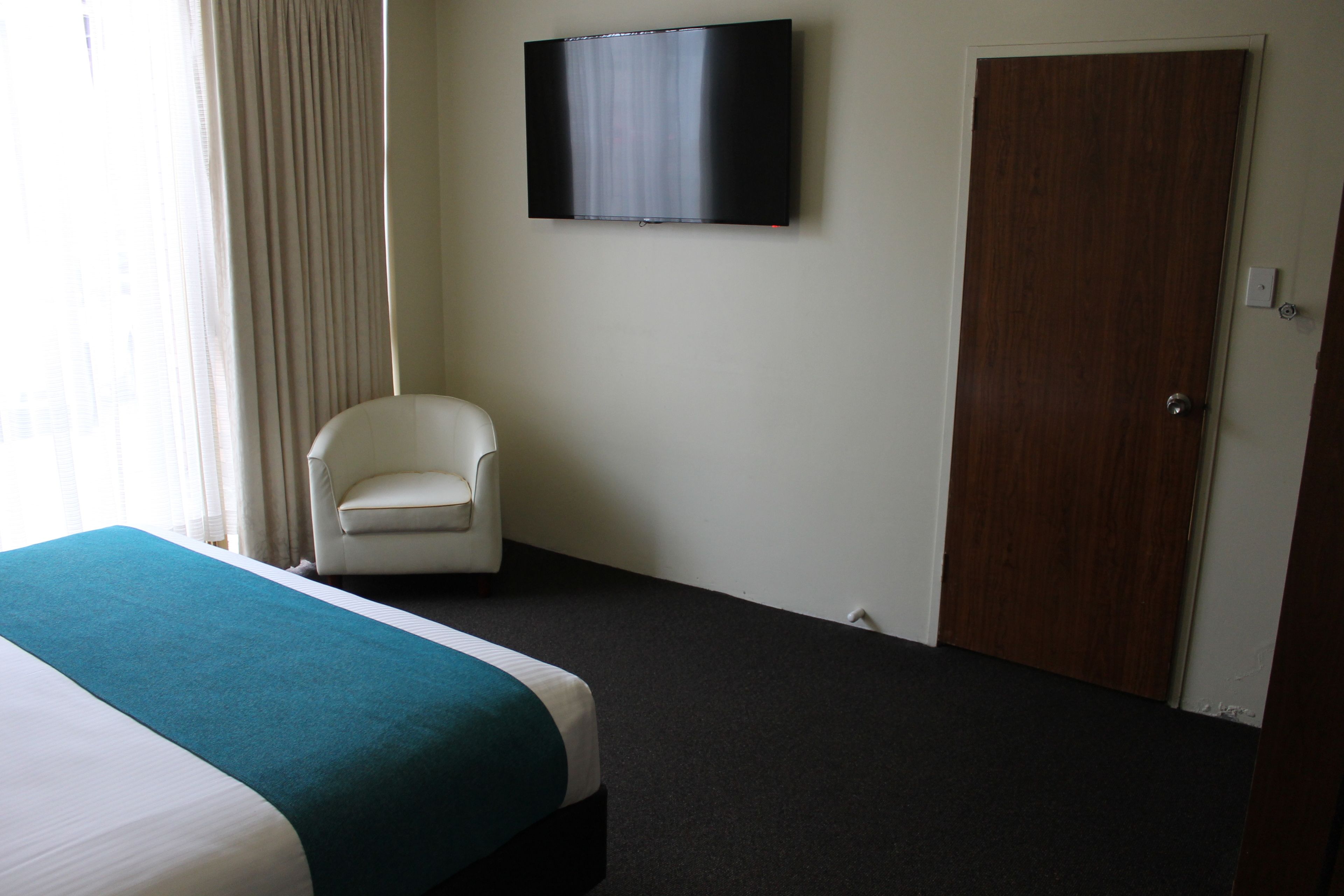 A hotel room with a bed, a chair, a television, and a door.