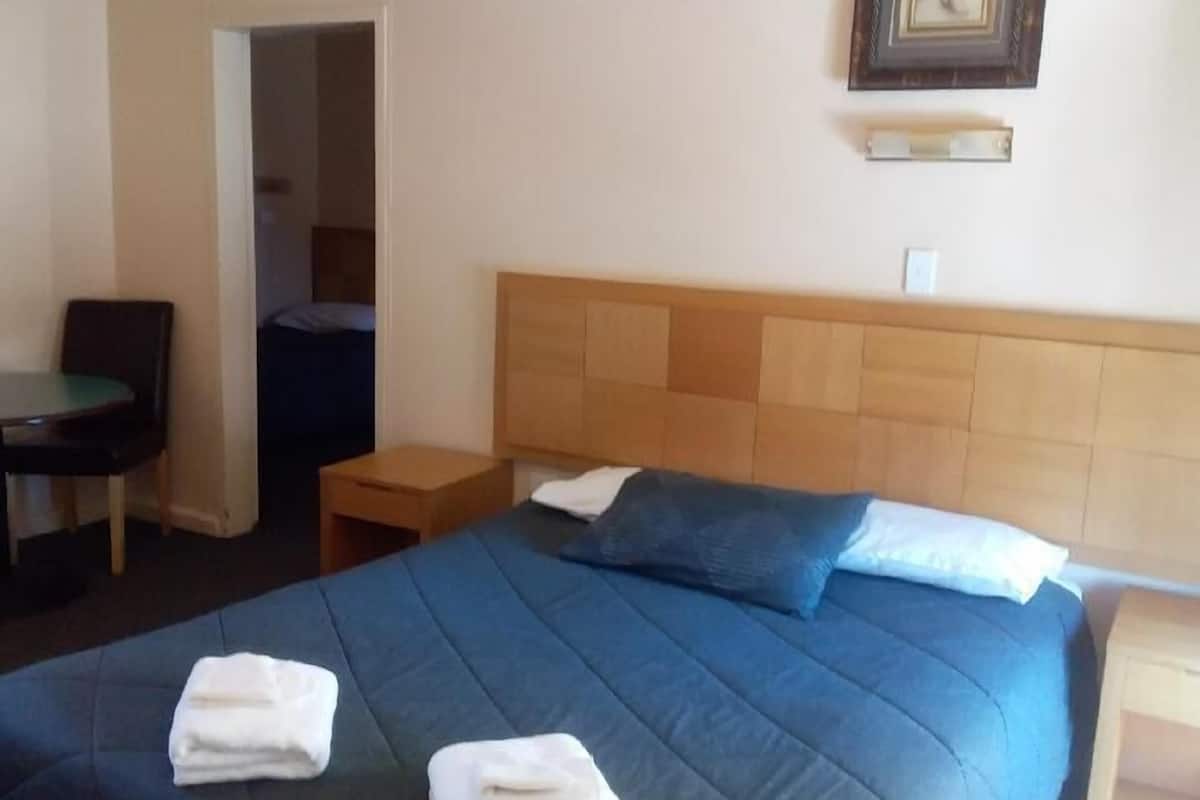 Quarto de hotel com cama, uma cadeira, mesa de cabeceira e um quadro na parede.