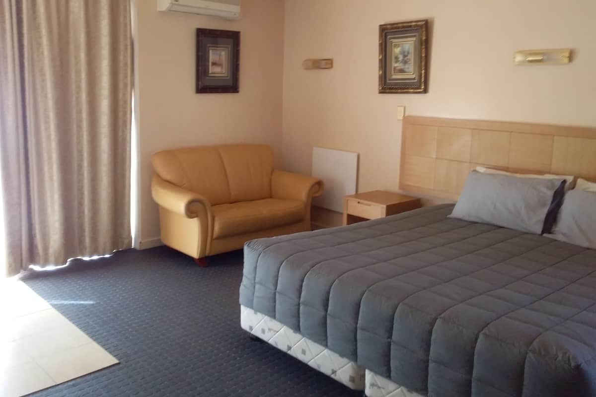 Quarto de hotel com cama, cadeira, mesa de cabeceira e ar-condicionado fixado na parede.