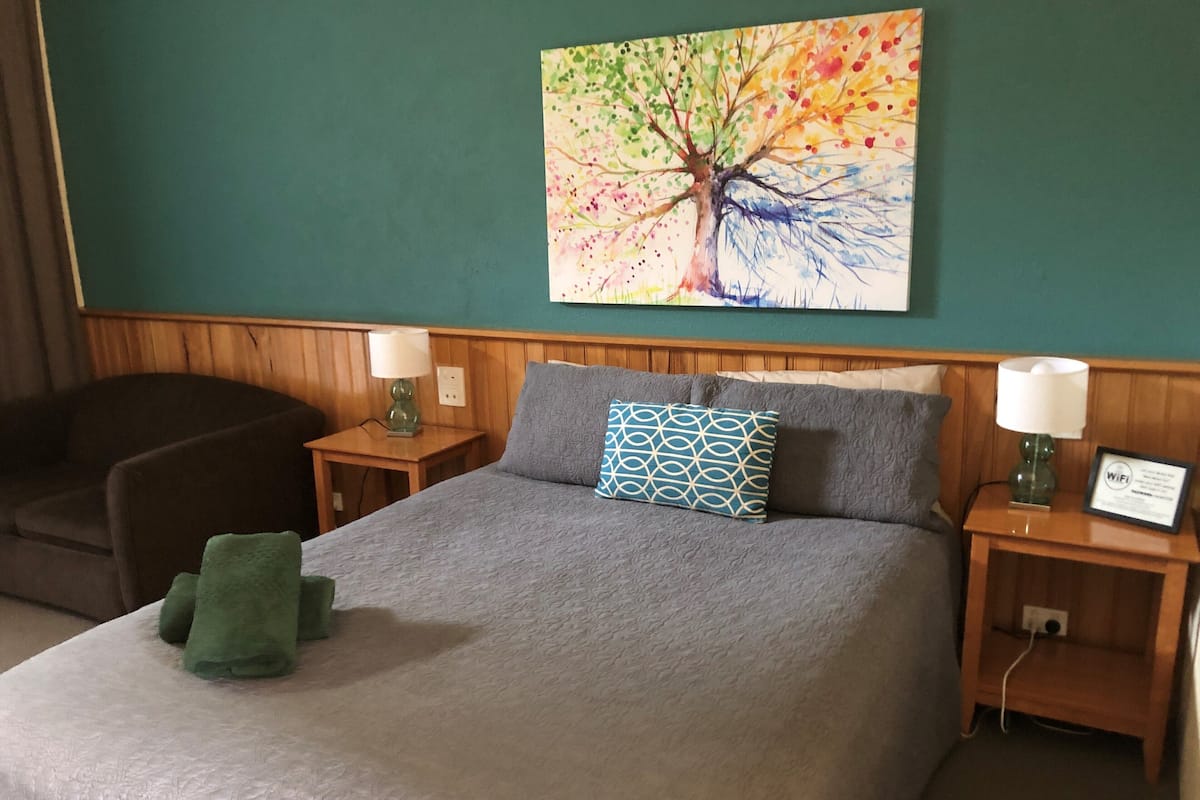 Ett hotellrum med en säng, två sängbord, en lampa, en tavla och en stol.