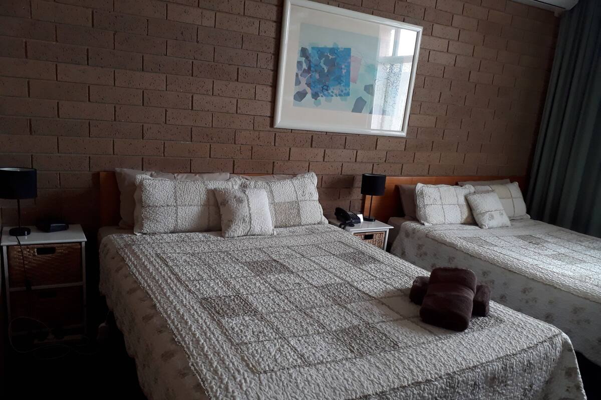 Ett hotellrum med två sängar, en tegelvägg, ett inramat konstverk och en nallebjörn på sängen.