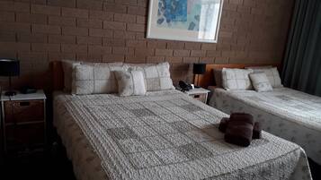 Ein Hotelzimmer mit zwei Betten, einer Ziegelwand, einem gerahmten Kunstwerk und einem Teddybären auf dem Bett.